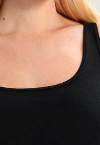 Débardeur noir à col arrondi, fabriqué en tissu extensible, avec une texture lisse et sans motifs ni embellissements visibles.