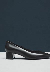 Pompa nera in pelle con punta affusolata e tacco basso a blocco. Superficie liscia e design elegante, caratterizzata da una silhouette minimalista.