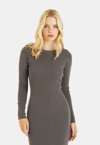 Vestido de punto gris con mangas largas, adornado con pequeños remaches decorativos en toda la tela, creando un aspecto texturizado.