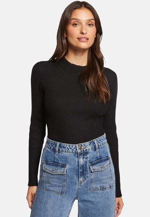Haut noir à manches longues côtelées avec un col montant, associé à un jean en denim bleu clair taille haute avec deux poches avant.
