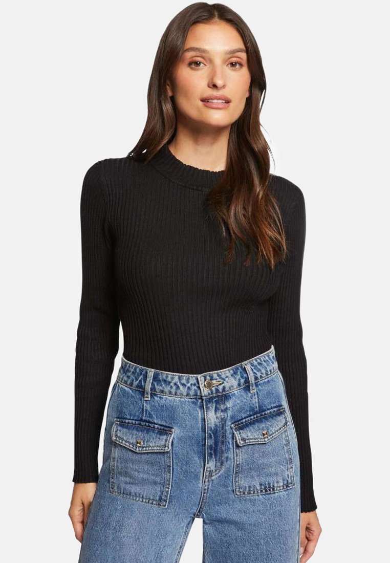 Haut noir à manches longues côtelées avec un col montant, associé à un jean en denim bleu clair taille haute avec deux poches avant.