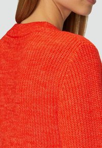 Helles rotes gestricktes Sweatshirt im Close-up, mit einem strukturierten Muster und sichtbaren Stichen, einem runden Halsausschnitt und einem gerippten Saum.