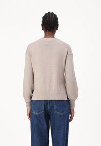 Maglione beige lavorato a maglia con scollo rotondo, polsini e orlo a coste, caratterizzato da una vestibilità ampia e maniche raglan. Indossato con jeans in denim blu.