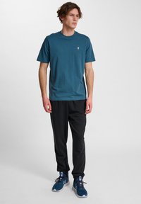 Blå bomullströja med rund hals, kombinerad med svarta sweatpants. Anmärkningsvärda detaljer inkluderar en liten logotyp på bröstet och sportskor.