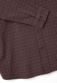 Camicia in flanella borgogna con un motivo a fantasia scacchi in nero e crema. Presenta polsini con bottoni e un orlo curvo. Tessuto testurizzato.