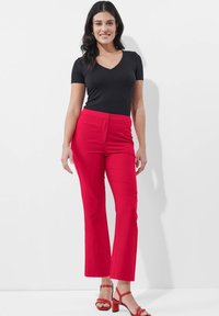 Zwart T-shirt met korte mouwen in combinatie met felrode geklede broek. De broek heeft een rechte pijp en twee voorklepzakken, gedragen met rode hoge hakken.