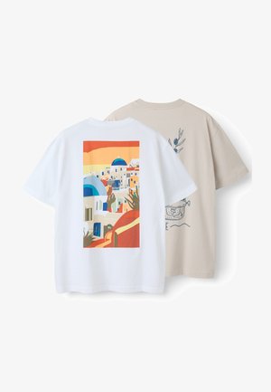 Zwei kurzärmelige T-Shirts, eines weiß mit einem bunten Druck eines mediterranen Dorfes, eines beige mit einer blauen botanischen und Topf-Illustration auf der Rückseite.