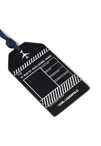 Czarna skórzana etykieta bagażowa z białymi wydrukowanymi polami informacji o locie, w paski wzór i granatowym paskiem. Wyświetla nazwę marki na dole.