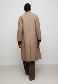 Brown wool coat with a relaxed fit, large notch lapel, and two side pockets. Features rolled sleeves and a simple seam detailing.