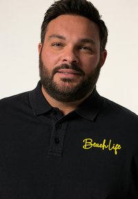 Černé polo tričko s žlutým logem "Beach Life" na levé straně, s klasickým límečkem a designem s knoflíkovou légou.