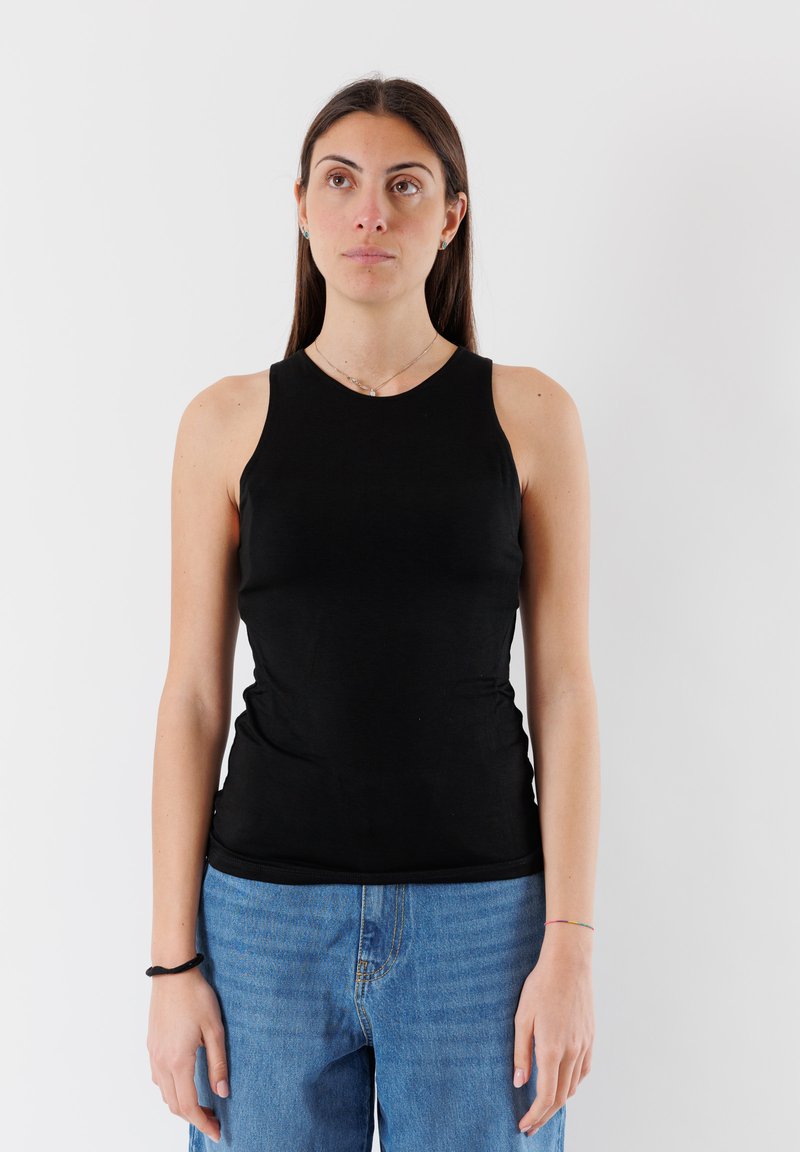 Canotta nera senza maniche realizzata in morbido cotone, con un design aderente e colletto alto, abbinata a jeans in denim blu chiaro.