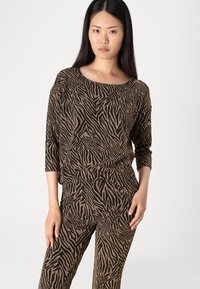 Ensemble haut et pantalon en imprimé animal noir et doré, avec une coupe décontractée, des manches à trois quarts et un tissu texturé avec un subtil éclat.