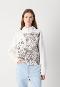 Felpa bianca con design a stampa leopardata, presenta un collo alto e maniche lunghe. Abbinata a jeans azzurri chiari.