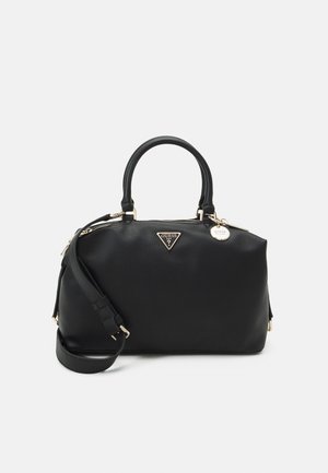 Sort Guess håndtaske i læder med to håndtag, aftagelig skulderrem, gyldent logo og rund metalvedhæng på ensfarvet baggrund.