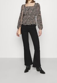 Blommönstrad svart topp med fyrkantig halsringning och puffärmar, kombinerad med högmidjade svarta flare-jeans och svarta klackiga stövletter.