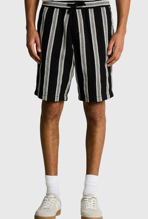 Man wearing black shorts with vertical white stripes, white crew socks, and beige sneakers, standing against a plain background.
