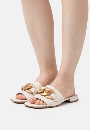 Infradito bianchi con una spessa catena dorata decorativa sulla parte superiore, suola piatta e design open-toe. Texture in pelle liscia.