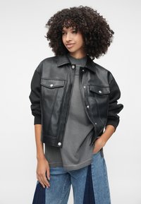 Mustast kunstnahast jakk, millel on kaks eesmist taskut, hõbedased detailid ja mustad kangast varrukad. Seljas halli toppi ja siniseid lapitöö teksaseid.