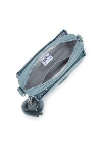 Light blue Kipling wallet, made of durable fabric, featuring two zippered compartments and a soft, fluffy pom-pom keychain detail.
