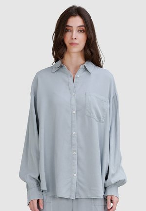 Jasnoniebieska, koszula zapinana na guziki o miękkiej fakturze i przedniej kieszeni. Posiada kołnierz oraz długie, luźne rękawy. Prosty design.