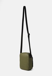 Olivengrøn rektangulær crossbody taske med en glat tekstur, justerbar sort rem og en lynlås-lomme på siden.