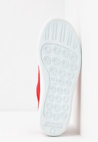 Semelle de chaussure blanche avec motifs circulaires antidérapants et taille 38, dessus en tissu rouge partiellement visible sur fond blanc.