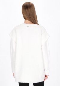 Biały, oversize sweter z miękkiej, teksturowanej tkaniny, z krótkimi, opadającymi rękawami i małym metalicznym akcentem z tyłu.
