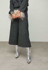 Pantalon large à fines rayures grises associé à des bottines argentées brillantes. Un sac à main gris clair duveteux et un bracelet manchette argenté complètent le look.