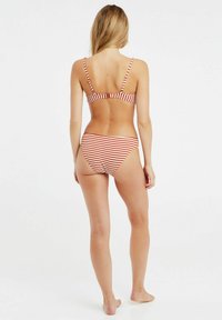 Czerwono-biały bikini w paski z dopasowaną górą w stylu braletki na cienkich ramiączkach oraz pasującymi, niskimi majtkami. Gładki materiał, casualowy design.