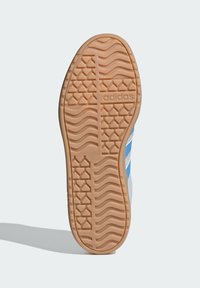 Adidas sneakersula i beige gummi med ett texturerat greppmönster, med blå ränder på de grå övre sidorna. "adidas"-logotyp präglad.