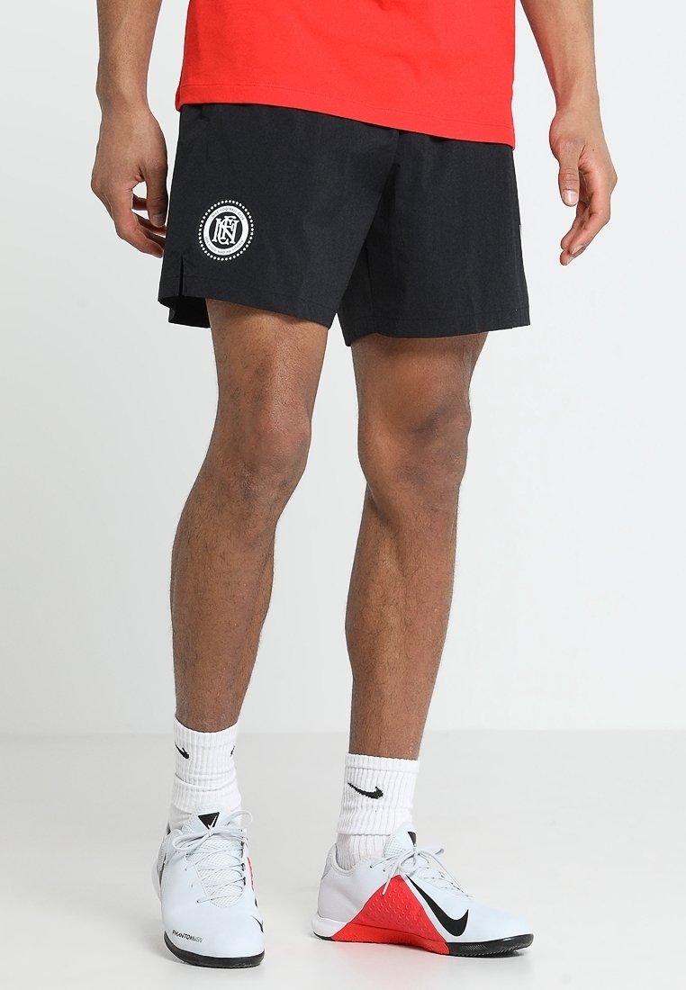 Mandlige ben iført sorte sports shorts med et hvidt logo, hvide Nike sokker og hvide Nike sports sko med røde og sorte detaljer.