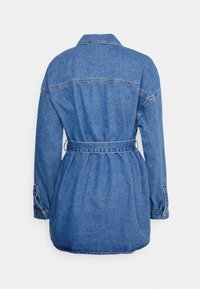 Blå denimjacka med lång ärm, krage och midjebälte, visad bakifrån på en vit bakgrund.