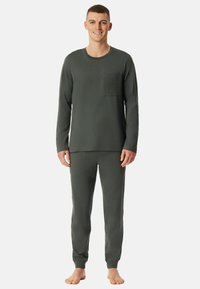 Conjunto de pijama para hombre en verde oscuro, hecho de tela suave, que incluye una camiseta de manga larga con un bolsillo texturizado y pantalones ajustados a juego.