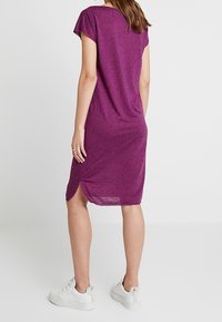 Lila, kortärmad, knälång klänning med en avslappnad passform och sidofickor, tillverkad av lätt, texturerad tyg. Bärs med vita sneakers.