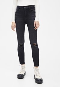 Jeans skinny de mezclilla negra con rodillas desgastadas, cintura alta y cinco bolsillos, combinados con botas blancas gruesas con cordones.