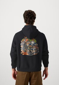 Zwarte hoodie met een kleurraf grafiek op de achterkant, die een botenscène afbeeldt met karakters, omgeven door water en bomen.