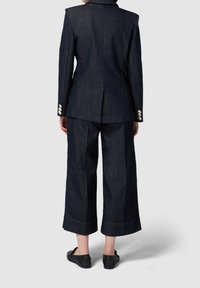 Tmavě modrý denimový oblek s přiléhavým sakem s širokými rameny, zadním rozparkem a širokými zkrácenými kalhotami s kontrastními švy.