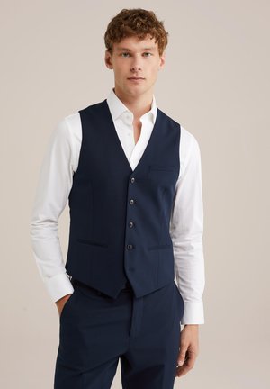 Navy waistcoat in smooth fabric with five buttons, slim fit, and two front pockets, worn over a white dress shirt.