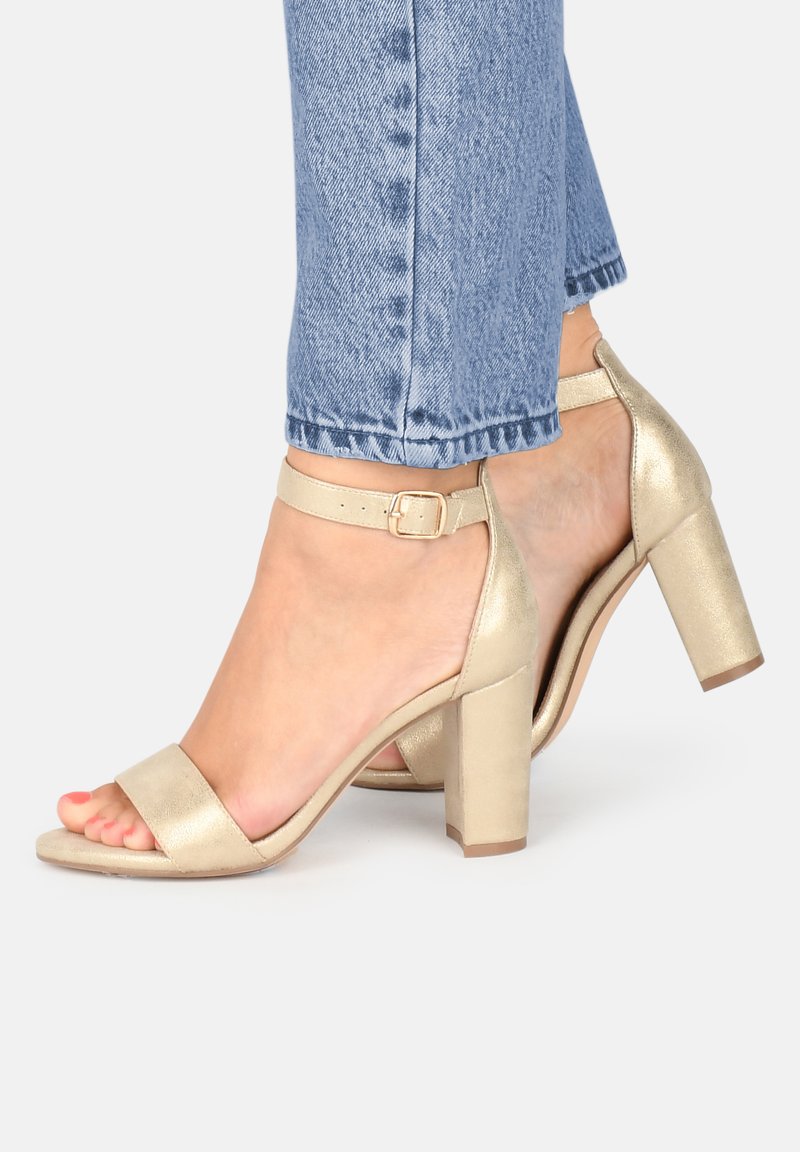 Goldene High-Heels-Sandalen mit einem breiten vorderen Riemen und einem Knöchelverschluss. Strukturiertes metallisches Finish, Blockabsatz und offenes Zehendesign.