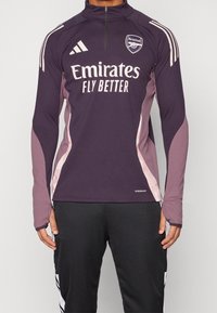 Langärmliges Sportoberteil in dunkelpurpur mit hellrosa Akzenten. Verfügt über einen hohen Kragen, einen Reißverschluss und das Arsenal-Logo auf der Brust.