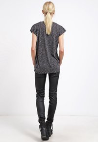 T-shirt grigio scuro testurizzato con maniche corte, abbinato a pantaloni in pelle nera lucida e stivaletti, visto da dietro.