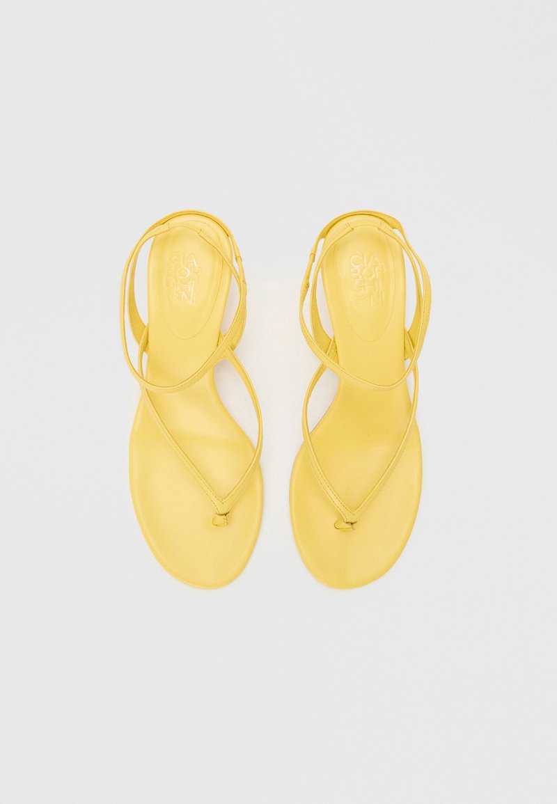 Sandalias amarillas con suela plana, que presentan tiras entrelazadas y una textura suave. Diseño minimalista sin herrajes o patrones adicionales.