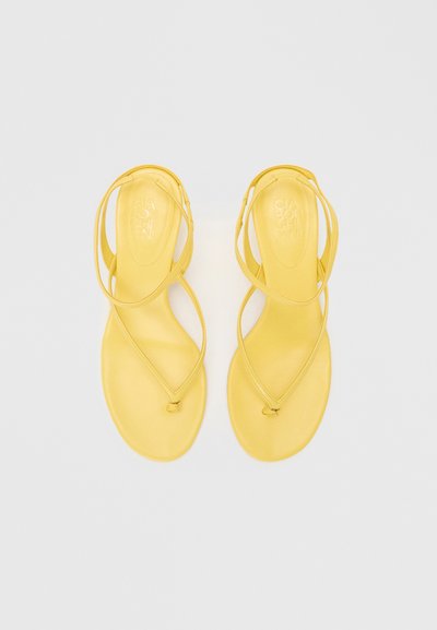 Žluté sandály s plochou podrážkou, s křížovými popruhy a hladkým povrchem. Minimalistický design bez dalších kovových částí nebo vzorů.