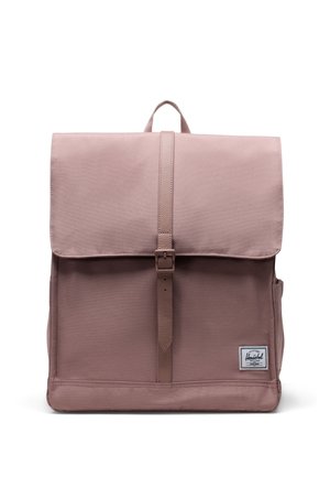 Light mauve Herschel backpack with flap closure secured by a vertical strap and buckle, featuring a side pocket and brand patch on front.