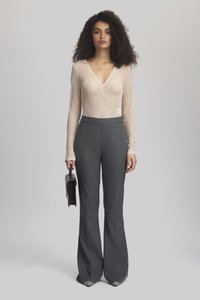 Light beige lace long-sleeve top with a deep V-neck paired with high-waisted gray tailored pants. Model holds a black handbag.