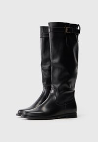 Botas de couro pretas até ao joelho com saltos baixos e correias de fivela ajustáveis perto do topo, apresentadas contra um fundo branco.