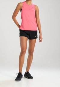 Top atletico senza maniche rosa abbinato a pantaloni corti neri e scarpe da corsa nere, con un design semplice e accenti del logo Nike.