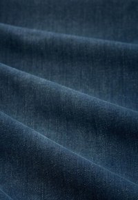 Donkerblauwe denimstof met een gladde textuur, met subtiele variaties in weving en kleur langs de gevouwen lagen.