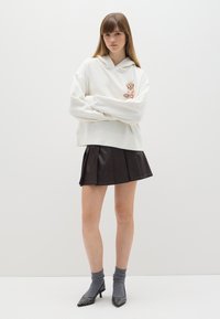 Witte hoodie met een hond graphic, gecombineerd met een zwarte geplooide leren rok, grijze sokken en zwarte puntige hakken met studs.