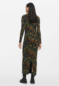 Virágmintás fekete ruha hosszú ujjakkal, narancssárga, lila és zöld mintákkal. Magas hasítóval és testhez simuló fazonban. Fekete csizmával viselték.